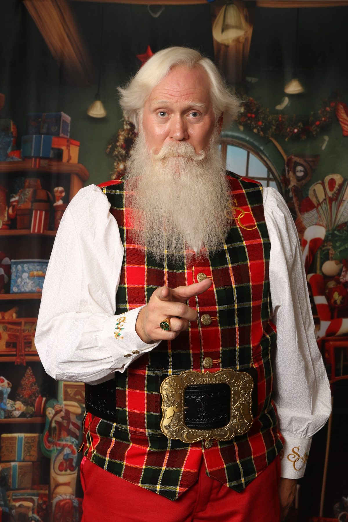 Santa Pat in a festive tartan vest, pointing playfully at the camera