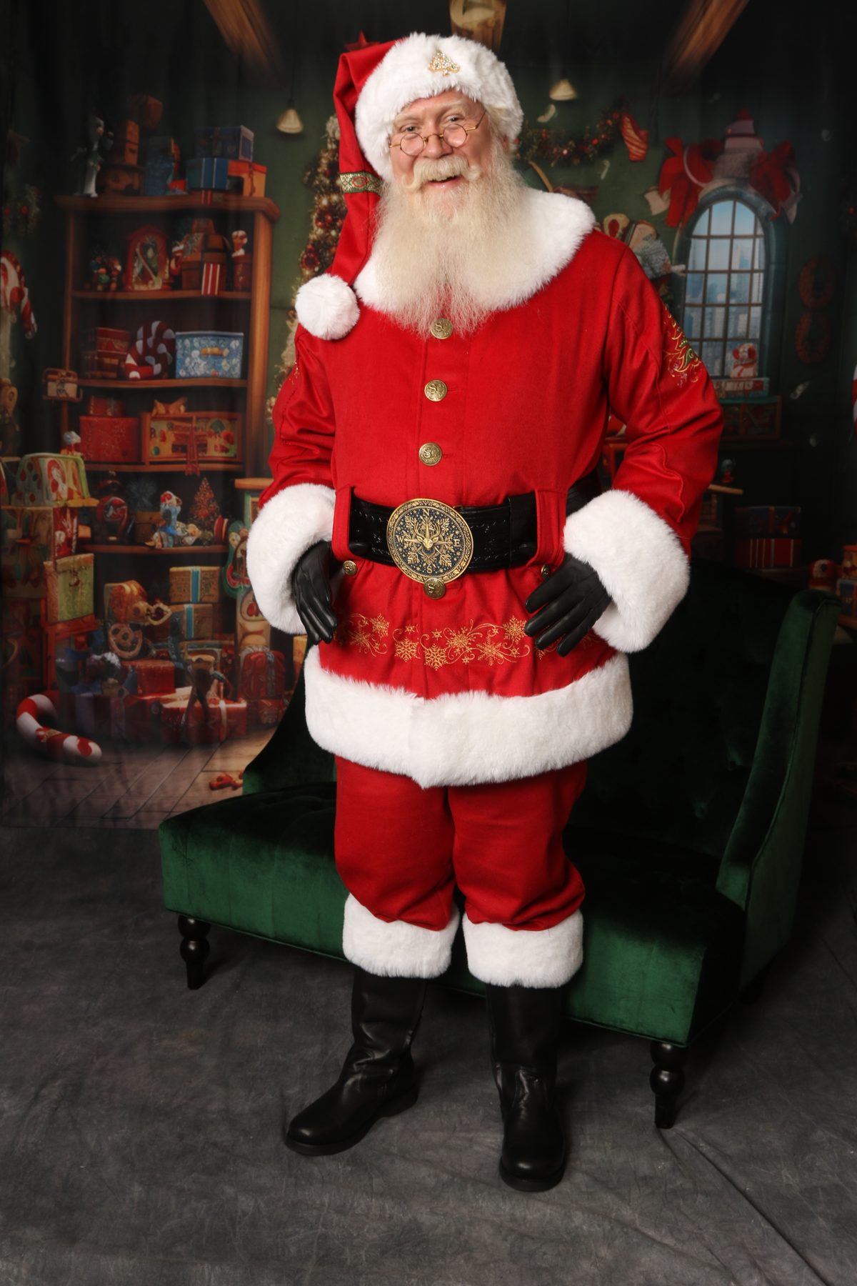 Santa Pat standing with hands on hips in his classic red suit with gold belt buckle, smiling warmly