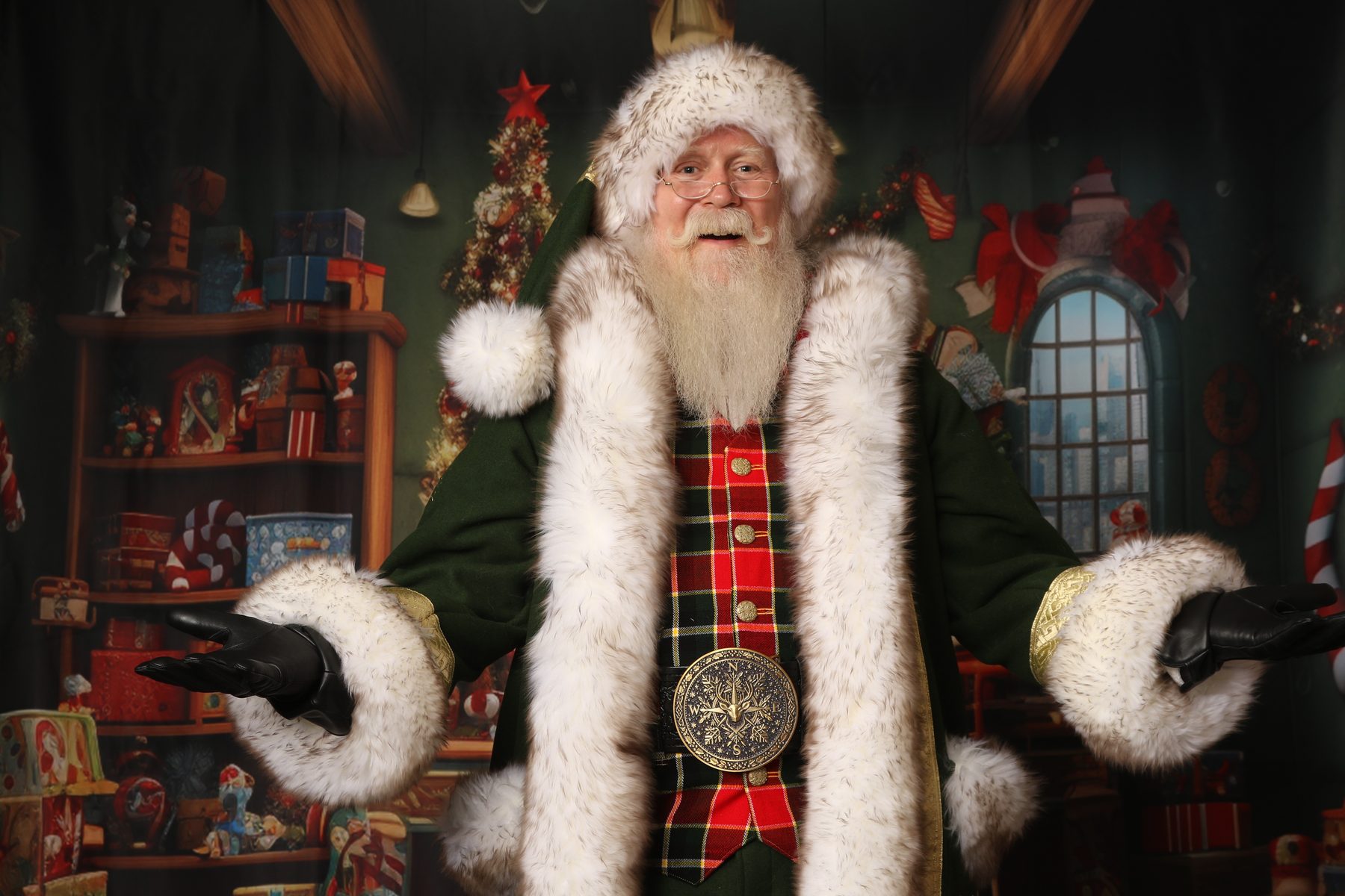 Santa Pat with open arms, smiling warmly in a green velvet coat with tartan vest